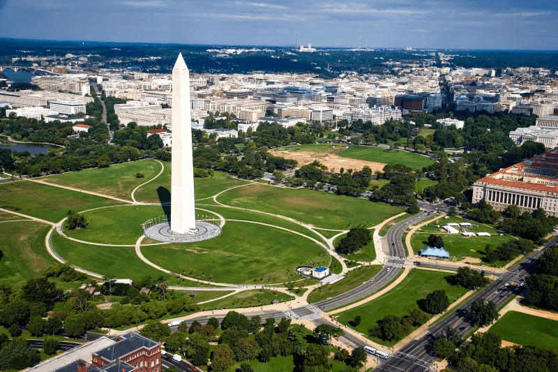 An aerial view of the Washington, DC, skyline, with the Washington Monument standing tall above a field of grass in the foreground